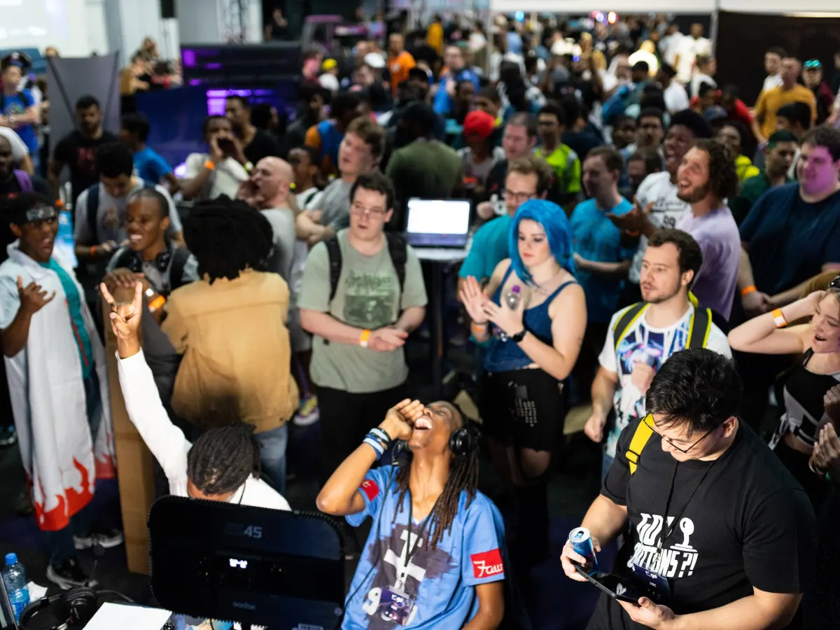 Players and spectators packed around a tournament station, one shouting at the screen